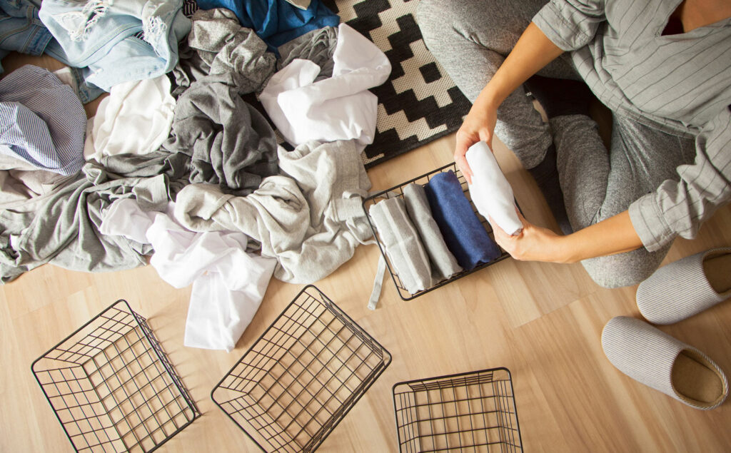 A woman folds her clothes and puts them in metal black baskets and boxes. Nordic style minimalism.